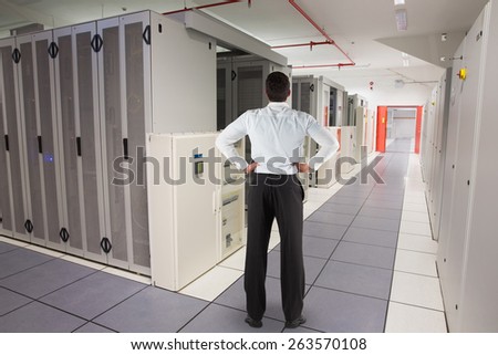 Businessman standing back to the camera with hands on hips against data center