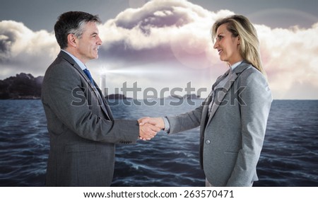 Pleased businessman shaking the hand of content businesswoman against calm sea with lighthouse
