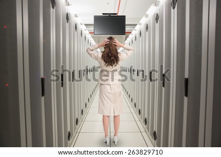 Businesswoman with hands on head standing back to camera against data center