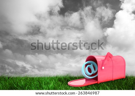 Red email post box against green grass under grey sky