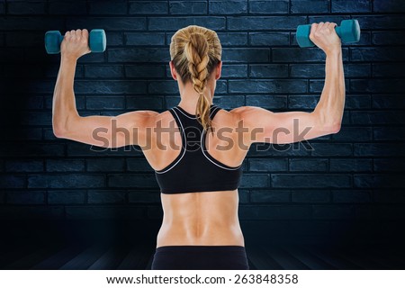 Female bodybuilder holding two dumbbells with arms up against black background