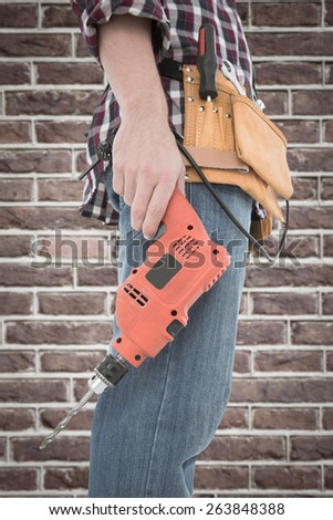 Male handyman holding drill machine against red brick wall