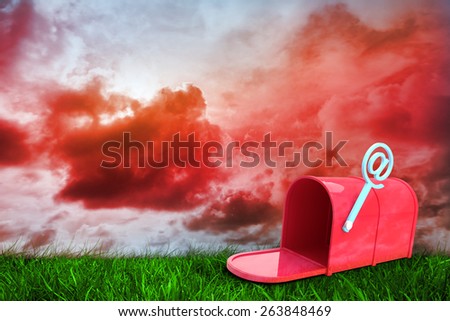 Red email post box against green grass under red cloudy sky