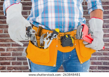 Midsection of handyman holding hand tools against red brick wall