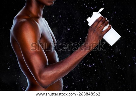 Mid section of a sporty young man holding protein drink against black background