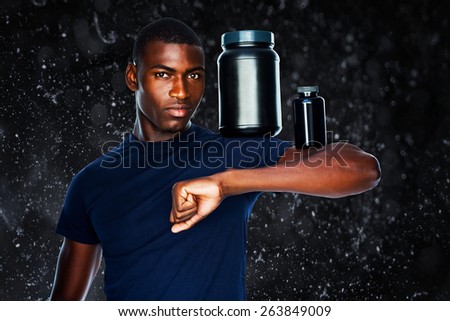 Fit man holding bottles with supplements on his biceps against black background