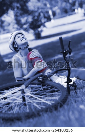 Young female bicyclist with hurt leg sitting on grass in the park