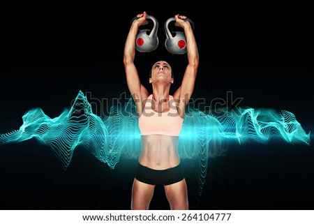 Serious female crossfitter lifting kettlebells above head against blue wave