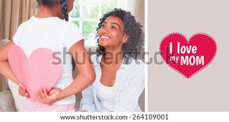 Pretty mother sitting on couch with daughter hiding heart card against mothers day greeting