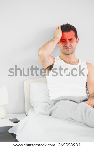 Grimacing handsome man having a headache in bright bedroom