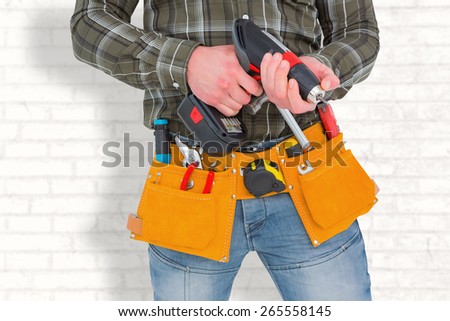 Manual worker holding gloves and hammer power drill against white wall