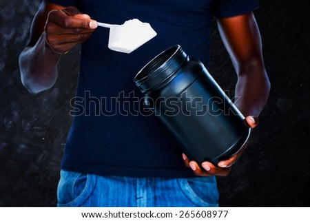 Mid section of man holding a scoop of protein mix against black background