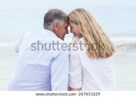 Happy couple sitting on the sand and smiling at each other at the beach