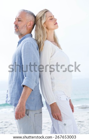 Happy couple standing back to back at the beach
