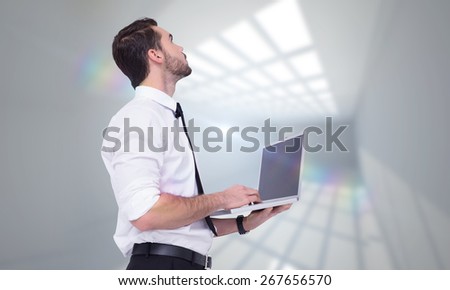 Sophisticated businessman standing using a laptop against room with windows at ceiling
