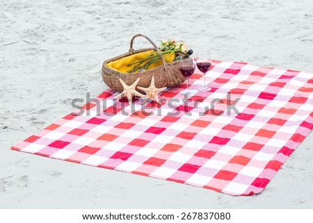 Picnic basket with glasses of red wine and starfishes on a blanket at the beach