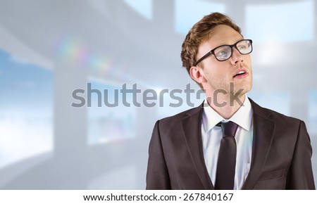 Young businessman thinking and looking up against bright white room with windows