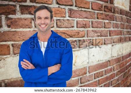 Happy mechanic with arms crossed over white background against red brick wall