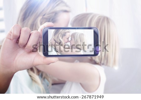 Hand holding smartphone showing against mother and daughter rubbing noses on sofa