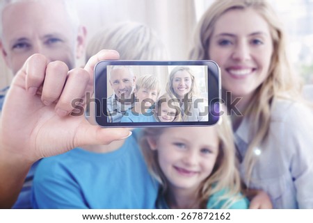 Hand holding smartphone showing against happy family smiling at camera