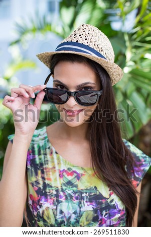 Smiling beautiful brunette wearing straw hat and sun glasses with palm tree behind her