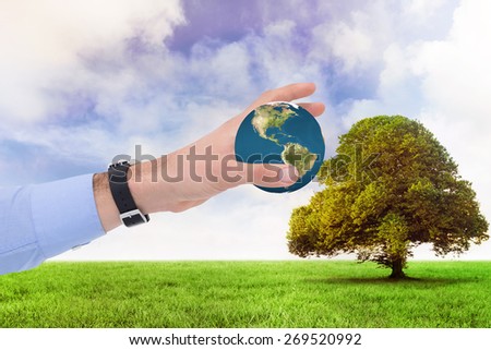 Businessman showing with his hand against tree in green field