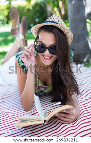 Smiling beautiful brunette lying and reading a book with palm tree behind her