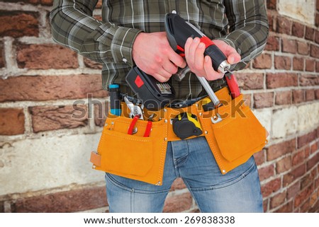 Manual worker holding gloves and hammer power drill against red brick wall