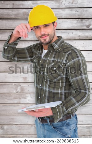 Smiling handyman writing on clipboard against digitally generated grey wooden planks