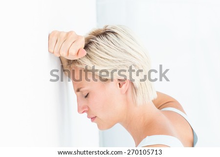 Sad blonde woman with her head on wall on white background