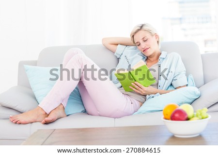 Pretty blonde woman reading a book on the couch in the living room