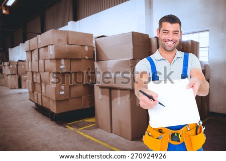 Smiling handyman giving clipboard for signature against cardboard boxes in warehouse