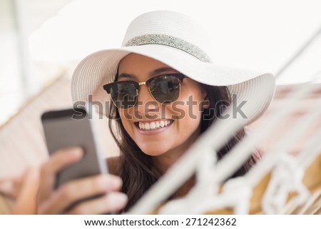 Pretty brunette relaxing on a hammock and texting with her mobile phone in patio