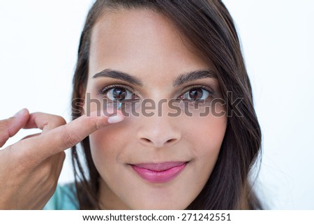 Beautiful woman applying contact lens on white background