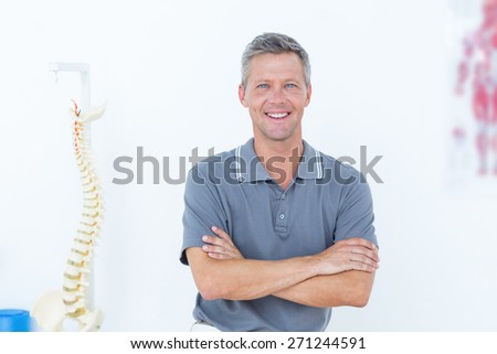 Smiling doctor standing arms crossed in medical office