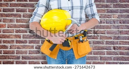 Technician holding hammer and hard hat against red brick wall