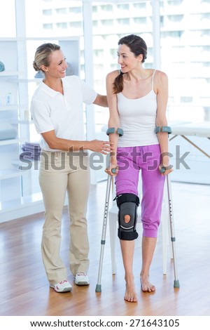 Doctor helping woman walking with crutches in medical office