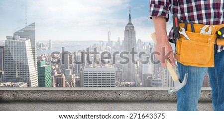 Repairman wearing tool belt while holding hammer against large city