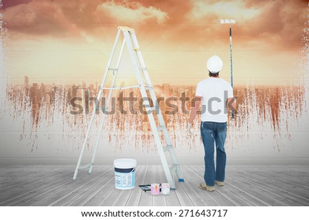 Man with paint roller standing by ladder against sun shining over city