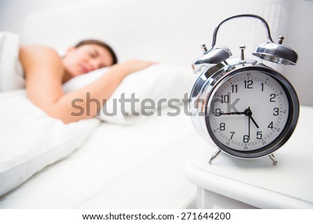 Pretty brunette sleeping in bed with alarm clock at home in the bedroom