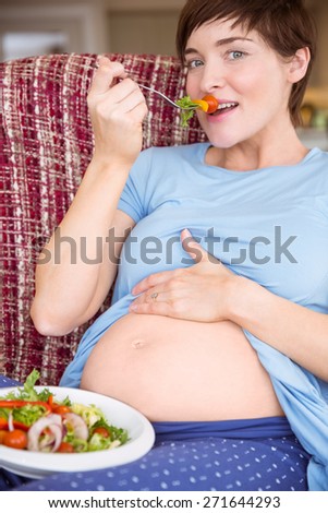 Pregnant woman eating a salad at home in the living room