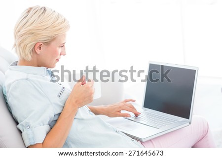 Pretty blonde woman using her laptop and holding mug in the living room