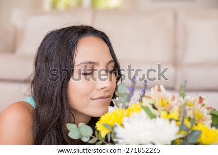 Pretty brunette lying on the floor and smelling the flowers at home in the living room