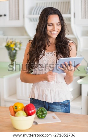 Pretty brunette using tablet pc and preparing salad in the kitchen