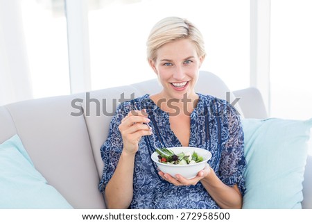 Pretty blonde woman eating bowl of salad in the living room
