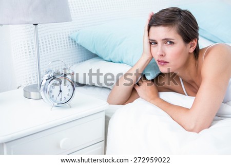 Beautiful young woman lying in bed with alarm clock at home in the bedroom