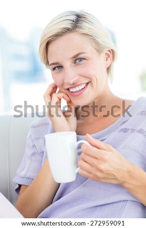 Pretty blonde woman sitting on the couch and holding a mug in the living room