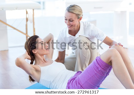 Trainer working with woman on exercise mat in medical office