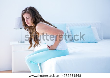 Pretty woman suffering from stomach pain at home in the bedroom