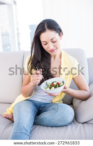 Pretty brunette eating salad on couch at home in the living-room